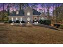 Beautifully lit home at dusk featuring a stone facade, arched windows, mature trees and manicured lawn at 4990 Sawgrass Nw Pl, Acworth, GA 30102