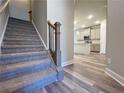 Carpeted staircase with dark wood banister leading to an open-concept kitchen and light colored floors at 5485 Rock Place Ct # 42, Norcross, GA 30093