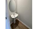 Compact powder room featuring a pedestal sink, oval mirror and wood-look floors at 111 Woodside Ct, Temple, GA 30179