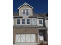 Attractive townhome boasts a two-car garage and appealing brick and siding accents under a clear blue sky at 1935 Manor Pointe Dr, Cumming, GA 30041