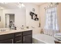 Bright bathroom featuring a double vanity, soaking tub, decorative shelving, and a window with elegant curtains at 3362 Brockenhurst Dr, Buford, GA 30519