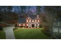 Exterior home view shows a well-lit brick house with a green lawn and side yard at dusk at 4000 Rockingham Dr, Roswell, GA 30075