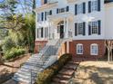 Inviting front entrance featuring a staircase with black railings, brick accents, manicured landscaping, and mature trees at 4399 Jett Nw Pl, Atlanta, GA 30327