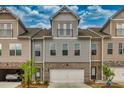 Townhome exterior with neutral siding, stone accents, individual garages, and mature landscaping under a partly cloudy sky at 2020 Manor Pointe Dr, Cumming, GA 30041