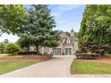 Beautiful home with a circular driveway leading to a three-car garage, mature trees and landscaping at 165 Ansley Way, Roswell, GA 30075