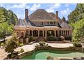 Expansive home back view featuring a covered patio, stone pool with a waterfall, and lush greenery at 8480 St Marlo Fairway, Duluth, GA 30097
