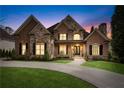 Beautiful brick and stone home featuring manicured lawn, circular driveway, and an inviting front porch at dusk at 8760 Colonial Pl, Duluth, GA 30097