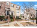 View of two-story tan sided townhouse with black door and shutters, brick stairs, and manicured yard at 1262 Park Pass Row, Suwanee, GA 30024