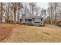 View of the gray home featuring a sloped lawn, mature trees, and a quaint front porch at 3332 Cottonwood Ln, Snellville, GA 30078