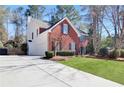 Side view of a well-maintained two-story brick home with white siding, large driveway, and landscaped lawn at 5569 Snowy Orchid Dr, Sugar Hill, GA 30518