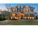 Beautiful two-story home featuring a stone facade, manicured lawn, and charming shuttered windows at twilight at 4440 Croftshire Pl, Cumming, GA 30040