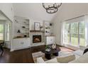 Bright living room features a stone fireplace, built-in shelving, dark hardwood floors and a modern chandelier at 5570 Rolling Oaks Dr, Cumming, GA 30040