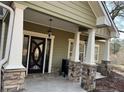 Inviting front porch with stone-based columns and a decorative glass front door at 10390 Rivertown Rd, Fairburn, GA 30213