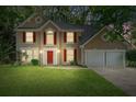 Exterior view of a well-lit two-story home on a verdant lawn at dusk at 7045 Threadstone Overlook, Johns Creek, GA 30097