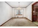 An empty dining room featuring carpeted floors, a window, a decorative chandelier, and floral wallpaper trim at 444 Wellington Way, Jonesboro, GA 30238