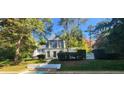 Two-story home featuring white brick, blue accents, and a lush landscape, as viewed from the pool at 499 Johnson Ferry Nw Rd, Atlanta, GA 30328