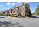 Corner view of a brick townhome complex featuring manicured landscaping, sidewalks, and neighborhood street, with a sunny sky above at 4406 Kendall Way, Roswell, GA 30075