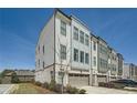 Stylish townhouse showcasing a gray and white facade, complemented by brick details, a garage, and lush landscaping at 6187 Kelly Carlin Way, Norcross, GA 30071