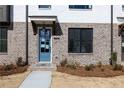 Close-up of townhome featuring blue door, brick facade, covered porch, and manicured landscaping at 1132 Larkin Dr # 34, Buford, GA 30518