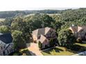 Aerial view of a two-story brick home surrounded by lush green trees and rolling hills at 5347 Harbury Cv, Suwanee, GA 30024