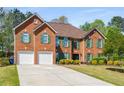 Attractive red brick home boasts an inviting driveway and well-maintained landscaping with green shutters, with a three-car garage at 308 Paper Woods Dr, Lawrenceville, GA 30046