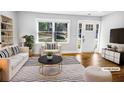 Bright, staged living room with large window, hardwood floors, white sofa and chair, and built in bookshelf at 1886 Hazelwood Se Dr, Marietta, GA 30067