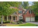 Charming brick home with a welcoming front porch and a two-car garage nestled among mature trees at 8355 Ainsworth Dr, Cumming, GA 30041