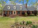All brick home showcasing dormer windows and a meticulous lawn accented by mature trees and a rock garden at 6695 Woodstock Rd, Acworth, GA 30102