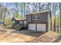 View of home's exterior with two-car garage and wooded setting at 477 Victoria Rd, Woodstock, GA 30189