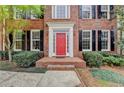 Up-close view of the brick facade highlighting the striking red front door and neat landscaping of the property at 10460 Cranchester Way, Alpharetta, GA 30022