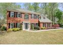 Charming two-story brick home with black shutters and a well-manicured front lawn surrounded by mature trees at 1010 Allenbrook Ln, Roswell, GA 30075