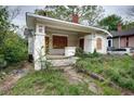 Exterior view of a distressed bungalow with boarded windows, overgrown vegetation, and a covered porch at 1366 Sylvan Sw Rd, Atlanta, GA 30310