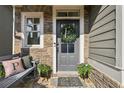 Welcoming front entrance featuring a gray door with wreath, stone accents, and a cozy bench with pillows at 8385 E Village School E Dr, Cumming, GA 30041