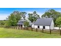 Quaint farmhouse featuring white siding, black roof, and a wooden fence, nestled among mature trees and green grass at 85 Carroll Slough Rd, Kingston, GA 30145