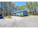 Blue home's exterior with long porch, natural setting, and gravel parking area on a sunny day at 5955 Kemp Dr, Acworth, GA 30102