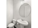 Clean, simple half bathroom features a pedestal sink, round mirror and a toilet with a modern design at 1395 Crestwind Nw Rd, Kennesaw, GA 30152