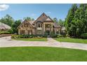 Elegant home with stone and brick exterior, circular driveway, and manicured lawn at 6935 Wakehurst Pl, Cumming, GA 30040