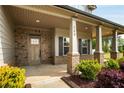 Inviting covered porch with stone accents and stately columns with a green and red manicured garden at 209 Brynn Ln, Mcdonough, GA 30252
