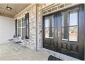 Inviting covered porch with stone accents featuring a double front door, chairs and side window at 4466 Woodland Bank Blvd, Buford, GA 30518