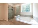 Bathroom with a tub and separate glass door shower featuring tile surround and a window offering natural light at 7505 Woolf Way, Cumming, GA 30028