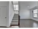 Staircase in a brightly lit foyer featuring hardwood floors, carpeted stairs, and white walls at 5530 Bower Pl, Cumming, GA 30028