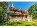 A beautiful two-story brick home with a turret and wraparound porch is surrounded by green grass and trees at 3593 Hemphill St, Atlanta, GA 30337