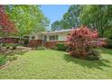 Landscaped front yard of a single-story home, featuring a brick facade, green lawn, and mature trees at 3800 Whitaker Ln, Lithia Springs, GA 30122