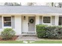 Close-up of a freshly painted gray front door with a wreath, flanked by green bushes and white brick at 1295 Lindenwood Ne Ln, Brookhaven, GA 30319