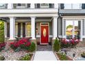 Charming front porch with stone accents, white pillars, and a vibrant red door surrounded by colorful flowers at 2582 Corey Park Dr, Loganville, GA 30052