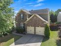 Two-story brick home with a two-car garage, surrounded by green lawn and mature trees creating a tranquil setting at 213 Roseman Way, Woodstock, GA 30188