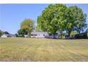Wide angle shot of an older, single story ranch home with light paint on a large, grassy lot and mature trees at 1312 Harbins Rd, Dacula, GA 30019