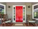 Inviting front porch with rocking chairs, a vibrant red door, and decorative lighting fixtures at 5876 Bridgemont Nw Pl, Acworth, GA 30101