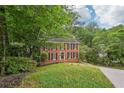 Red brick two-story house with black shutters nestled among mature trees and greenery at 2895 Shurburne Dr, Alpharetta, GA 30022