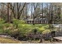 Brick home with lush front yard showcasing mature trees, creek, and landscaping at 1351 Stephens Sw St, Lilburn, GA 30047